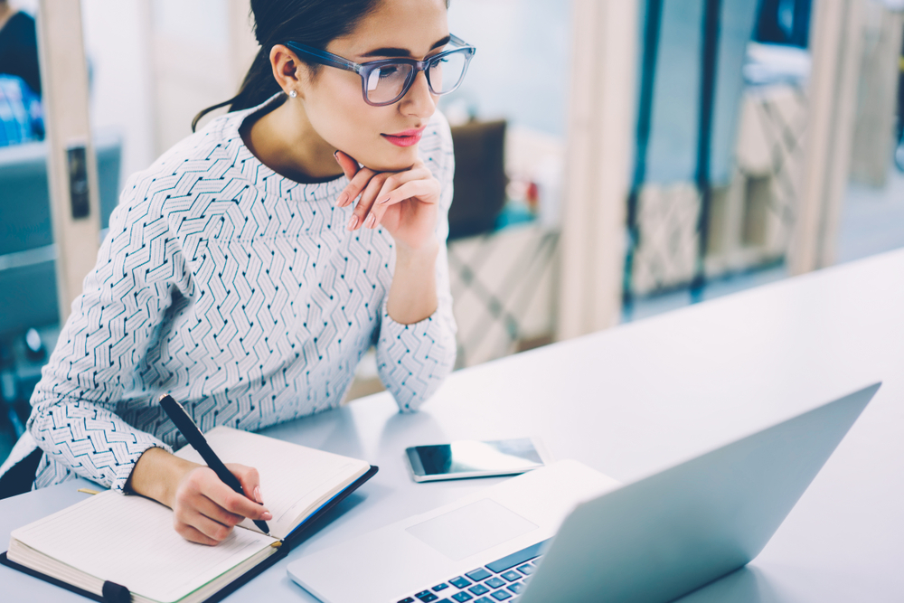 A young woman takes notes from her laptop.